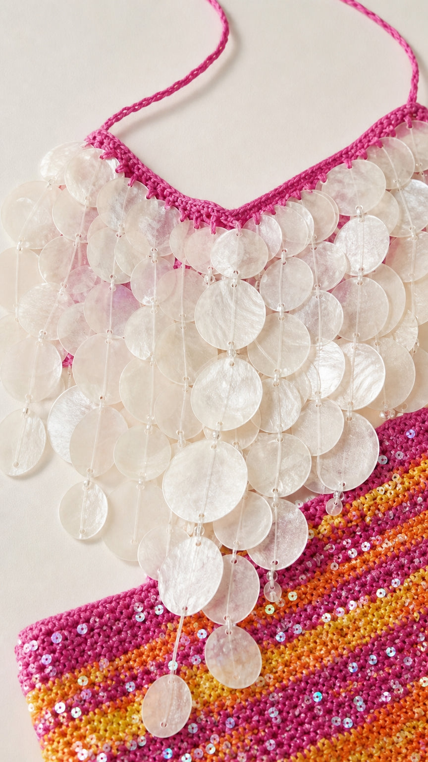 Close-up detail of iridescent round shell paillettes on crochet trim and sequined knit fabric