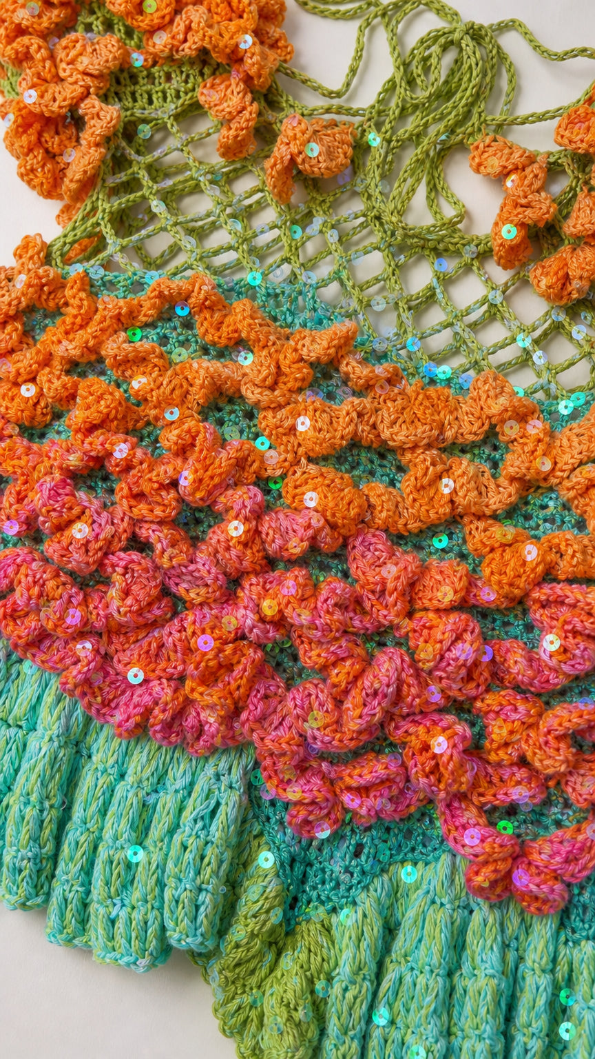 Close-up texture of 3D crochet knit pattern with sequin accents and ruffled green hem